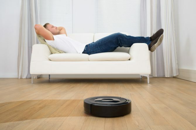 Άνδρας χαλαρωτικό στον καναπέ με ρομποτική ηλεκτρική σκούπα στο πάτωμα σκληρού ξύλου